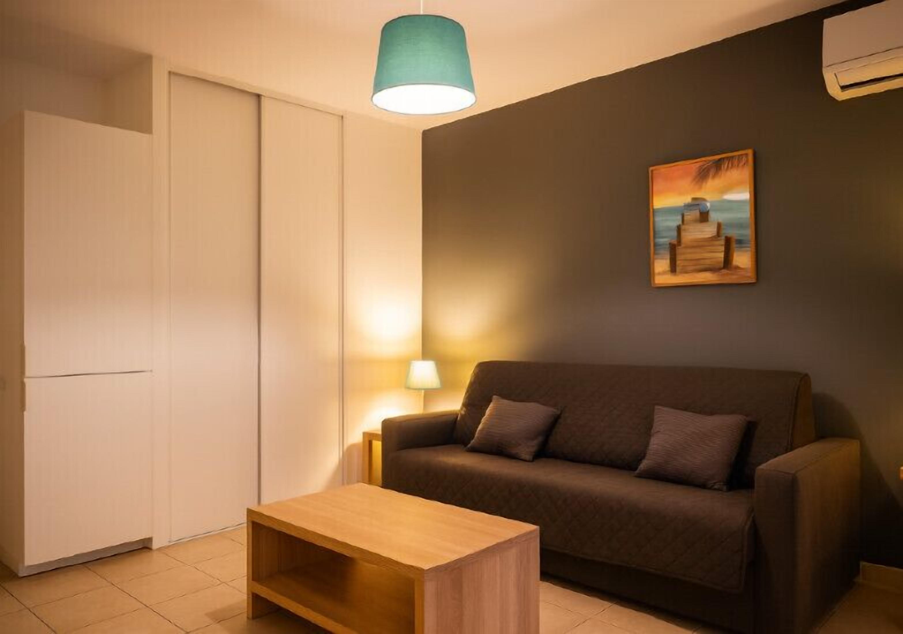 Uma sala de estar com sofá, mesa de centro, luminária e um quadro na parede.