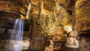Eine Höhle mit Stalaktiten, einem Wasserfall und einem Wasserbecken.