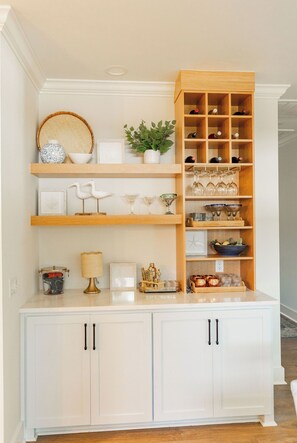 A white cabinet with black handles, shelves with decorative items, and a wooden display unit with wine glasses. - New! Cottage with pool near pier village! (St Simons Island)