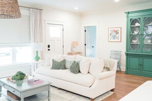 A living room with a white sofa, a green cabinet, and a window with curtains. - New! Cottage with pool near pier village! (St Simons Island)