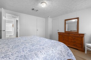 Ein Schlafzimmer mit Bett, Schminktisch, Spiegel und weißen Wänden.