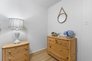 Ein Zimmer mit einem Holzkoffer, einer Lampe, einem Spiegel und einer Vase mit Blumen.