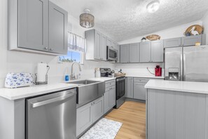 A modern kitchen with grey cabinets, stainless steel appliances, and a white countertop. - Hatchee Haven - Home in Steinhatchee (Steinhatchee)