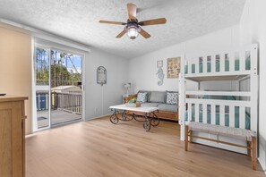 A room with a ceiling fan, a white bunk bed, a sofa, a coffee table, and a view through a glass door. - Hatchee Haven - Home in Steinhatchee (Steinhatchee)