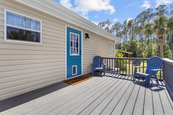 Ein Mobilheim mit einer Terrasse, zwei blaue Adirondack-Stühle und einer Tür mit Fenster.