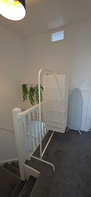 Eine Treppe mit weißer Geländer, einem aufgehängten Wäscheständer und einem kleinen Fenster darüber.