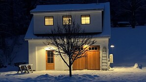 A two-story house with a snow-covered lawn, a wooden deck, and a garage.