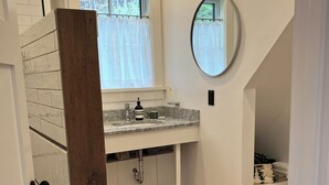 A modern bathroom with a marble sink, a round mirror, and a wooden door frame.
