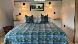 A bedroom with a checkered bedspread, two pillows, a framed picture on the wall, and two wall-mounted lamps.