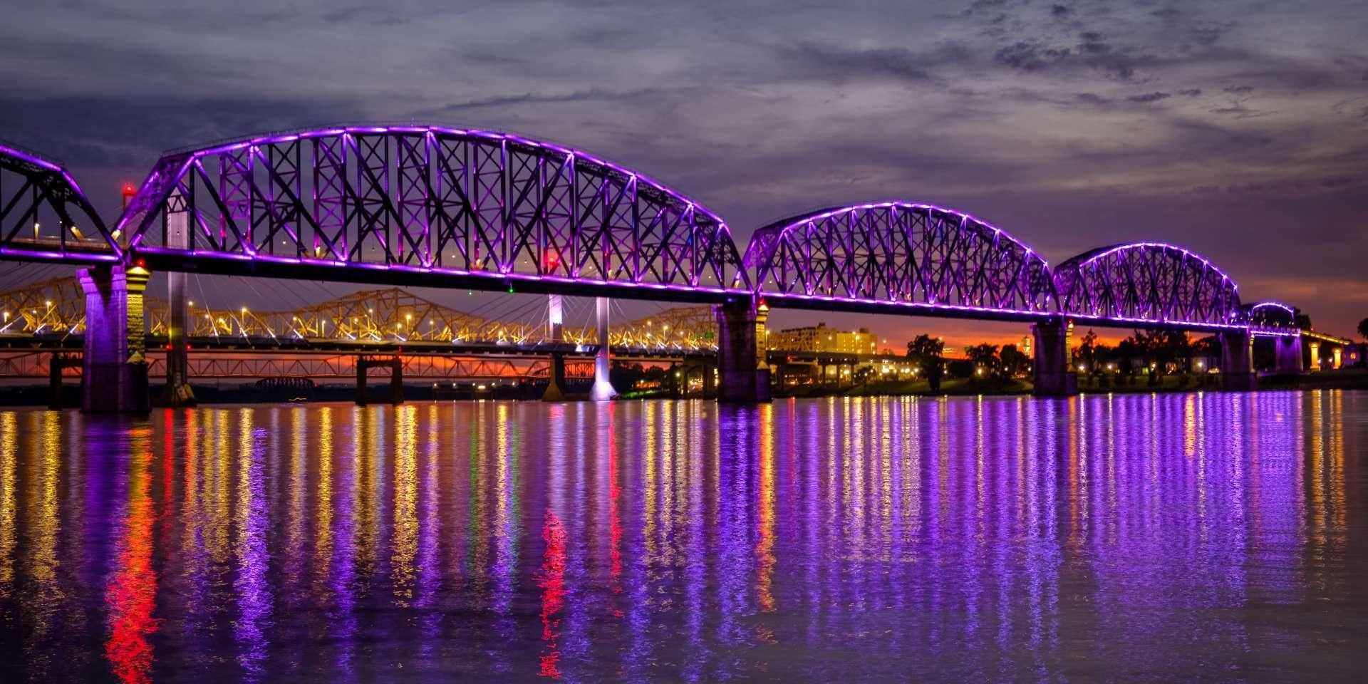 A bridge with a truss design and illuminated purple lights.