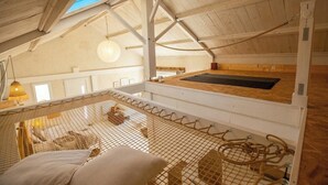 Um quarto no sótão com teto de madeira, luminária pendente, tela mosquiteira e plataforma de madeira.
