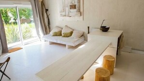 Quarto minimalista com uma grande mesa branca, banquetes de madeira, luminária pendente e vista através de uma porta de vidro.