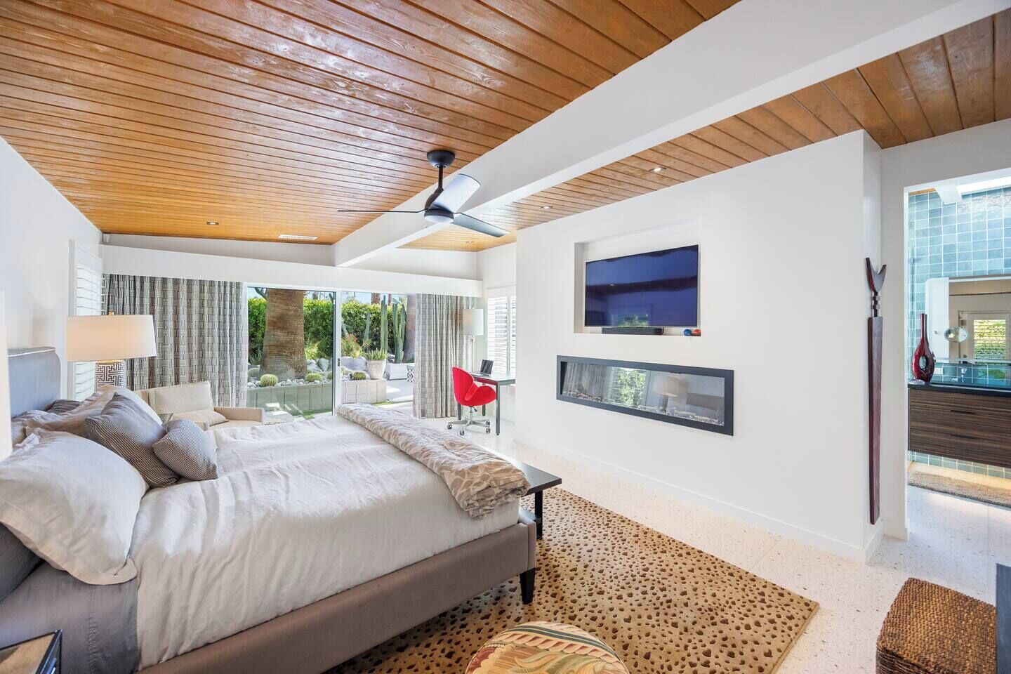 A modern bedroom with a large bed, a desk, and a TV mounted on the wall.