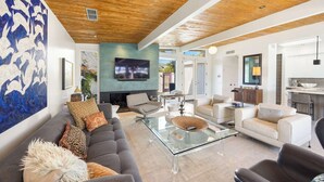 A spacious living area with a modern design, featuring a large sofa, a glass coffee table, and a flat-screen TV mounted on the wall. - Luxury Resort Oasis | New Pool, Spa, Fire Pit, EV (Palm Springs)