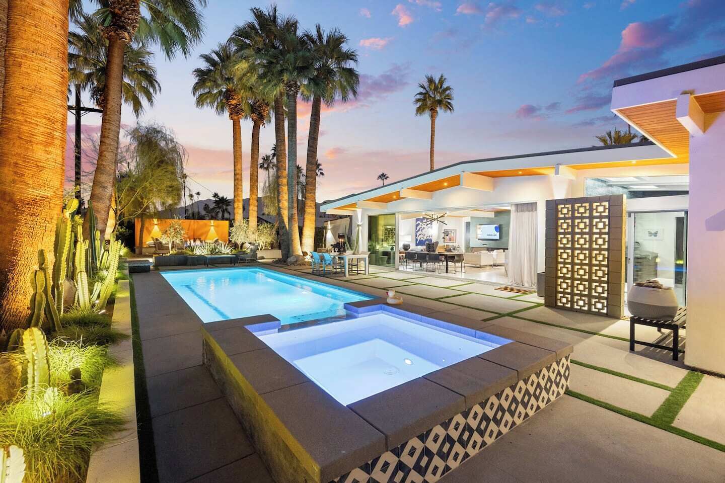 Ein modernes Haus mit Swimmingpool, Palmen und einem gut beleuchteten Außenbereich.