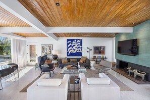 Ein modernes Wohnzimmer mit Holzboden, einem großen abstrakten Gemälde, einem Kamin und einem Flachbildfernseher.