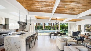A modern kitchen with a marble island, a dining area with a pool view, and a living room with a black armchair. - Luxury Resort Oasis | New Pool, Spa, Fire Pit, EV (Palm Springs)