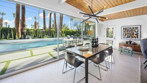 A modern interior with a dining area, a pool, and a view of palm trees. - Luxury Resort Oasis | New Pool, Spa, Fire Pit, EV (Palm Springs)