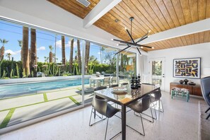 Ein modernes Interieur mit Essbereich, Pool und Blick auf Palmen.