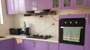 Et køkken med lilla skabe, en gasblus, en mikrobølgeovn og en kaffemaskine.