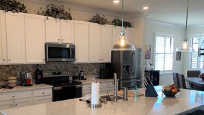 A modern kitchen with white cabinets, a large island with bar stools, stainless steel appliances, and pendant lighting. - SARASOTA NATIONAL - SEASONAL RENTAL -WITH GOLF MEMBERSHIP FOR 2 - 3 BR/2 BATH (Venice)