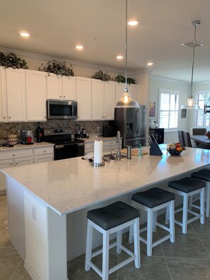 A modern kitchen with white cabinets, a large island with bar stools, stainless steel appliances, and pendant lighting. - SARASOTA NATIONAL - SEASONAL RENTAL -WITH GOLF MEMBERSHIP FOR 2 - 3 BR/2 BATH (Venice)