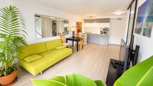 A living room with a sofa, a dining table with chairs, a kitchen area, and a large mirror. - Furnished Waikiki 1BR • Pet-Friendly • Utilities Included • Walk to Beach (Honolulu)