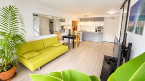 Ein Wohnzimmer mit einer Couch, einem Esstisch mit Stühlen, einer Küchenzeile und einem großen Spiegel.