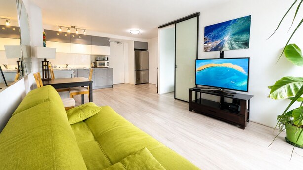 A modern living room with a sofa, a flat-screen TV, and a dining area with a table and chairs. - Furnished Waikiki 1BR • Pet-Friendly • Utilities Included • Walk to Beach (Honolulu)