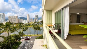 A balcony with a view of a city skyline, a body of water, and a green couch. - Furnished Waikiki 1BR • Pet-Friendly • Utilities Included • Walk to Beach (Honolulu)