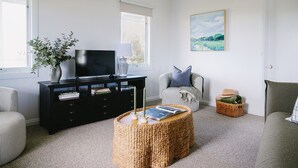 A living room with a black entertainment unit, a television, a wicker coffee table, and a striped armchair. - Suma Park Estate (Marcus Hill)