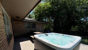 A hot tub in a backyard with a brick wall, a window, and a wooden table. - Gulfside Getaway Awaits (Corpus Christi)
