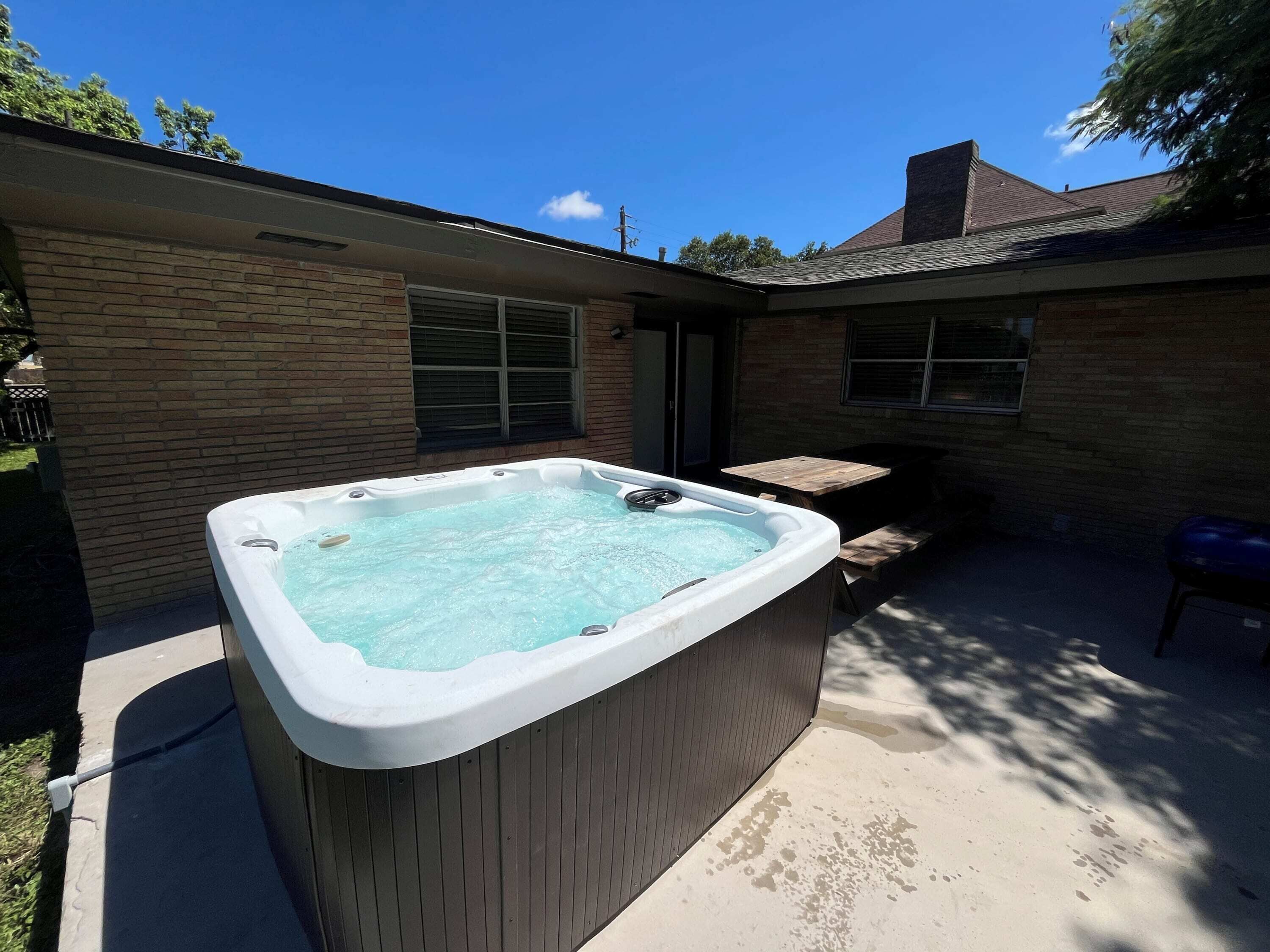 Ein Whirlpool in einem Garten mit einem Ziegelhaus, einer Holzterrasse und einem kleinen Tisch.
