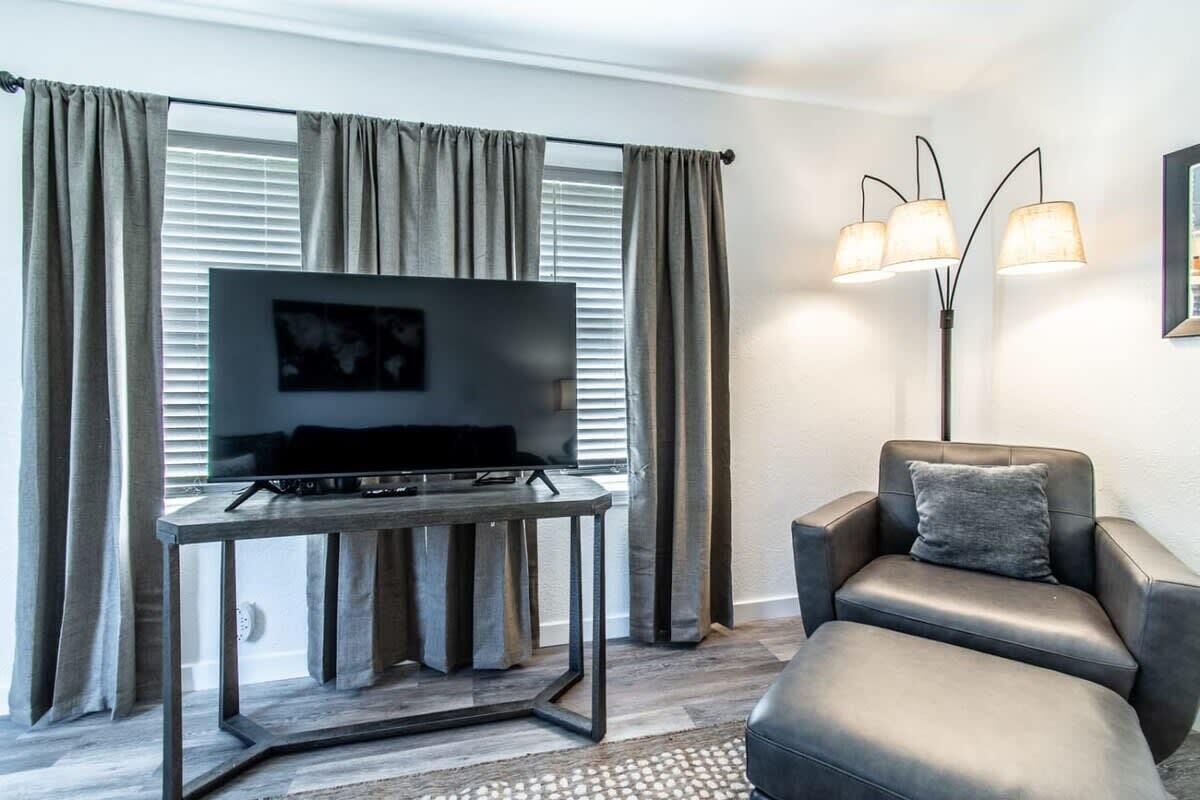 En moderne stue med et fladskærms-tv på et træbord, en læderlænestol og en gulvlampe.