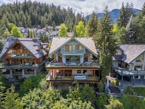 Ein großes, mehrstöckiges Chalet mit einem markanten Balkon, umgeben von dichtem Wald und Bergen.