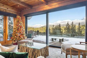 Ein modernes Interieur mit einem Glastisch, Holzboden und einem großen Fenster mit Blick auf eine verschneite Landschaft.