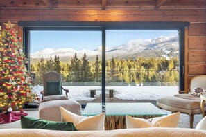 Ein gemütliches Cabin-Interieur mit großem Fenster mit Blick auf eine verschneite Berglandschaft.