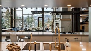 A modern kitchen with a large island, stainless steel appliances, and a view of snow-covered mountains. - Two Cedars - Ski in-Ski out, Kadenwood Estate (Whistler)