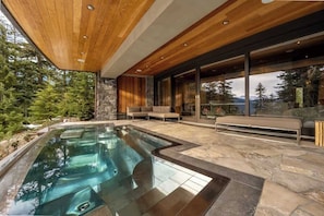 Ein moderner Poolbereich im Freien mit Steinböden, Holzbalkendecke und Blick auf Bäume.