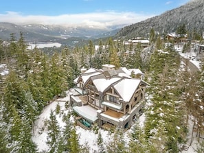 Ein großes, mehrgeschossiges Holzhaus mit Skilift, umgeben von schneebedeckten Bäumen und Bergen.