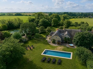 Una casa grande con piscina, rodeada de exuberante vegetación y campos.