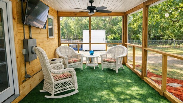 A covered patio with wicker chairs, a table, and a ceiling fan.