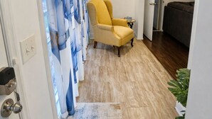 A hallway with a yellow chair, a blue and white curtain, a framed picture on the wall, and a plant.