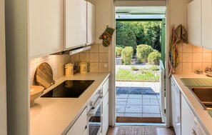 A kitchen with white cabinets, a wooden chair, and a view of a garden through the door. - 3 bedroom beautiful home in Gilleleje (Gilleleje)