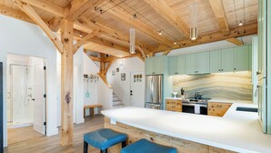 A modern kitchen with a large island, wooden beams, and light green cabinets.