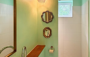 Ein Badezimmer mit einem Holzwaschtisch, zwei Wandspiegeln, einem Toilettenpapierhalter und einem Fenster mit Blick auf Bäume.