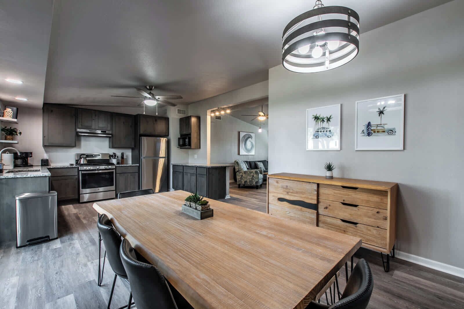 A modern kitchen with dark cabinets, stainless steel appliances, and a wooden dining table with chairs.