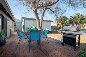 A backyard with a wooden deck, a barbecue grill, and a dining table with chairs. - Hinman Haven + Hot tub (Corpus Christi)