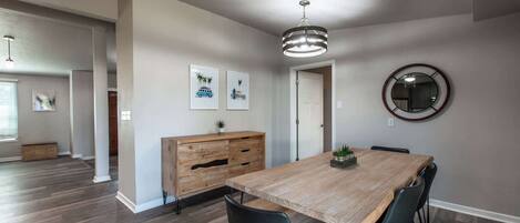 Ein Esszimmer mit Holztisch, schwarzen Stühlen, einer Holzkommode und gerahmten Bildern an der Wand.