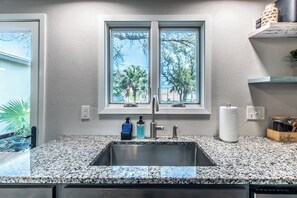 Eine Küche mit einer Arbeitsplatte aus Granit, einer Spüle aus Edelstahl und einem Fenster mit Blick auf Bäume.